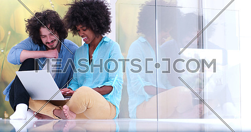 Young beautiful multiethnic couple using a laptop and doing shopping online while sitting on the floor