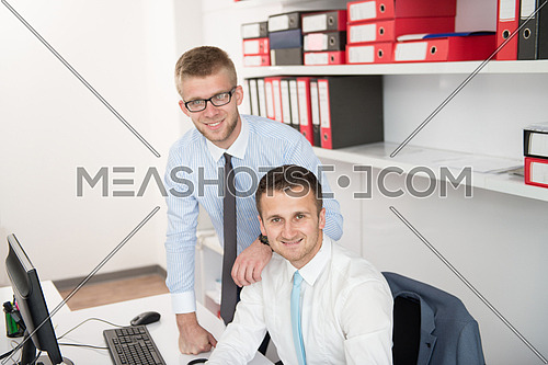 Two Businessmen In An Office Smiling At The Camera While Working Together Behind A Laptop Computer