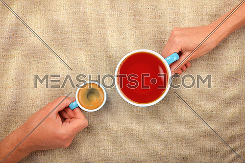 Different habits, two hands, man and woman, holding full cups, small espresso coffee and big black tea, together over linen canvas background