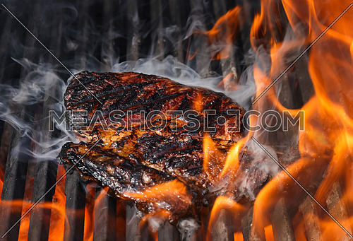 Close up searing and smoking ribeye beef steaks on open fire outdoor grill with cast iron metal grate, high angle view