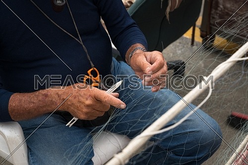 Old fisherman reparing fishing net.