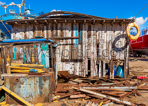 Shabby small building among lot of board with old orange life saver on edge of roof and clear blue sky on background