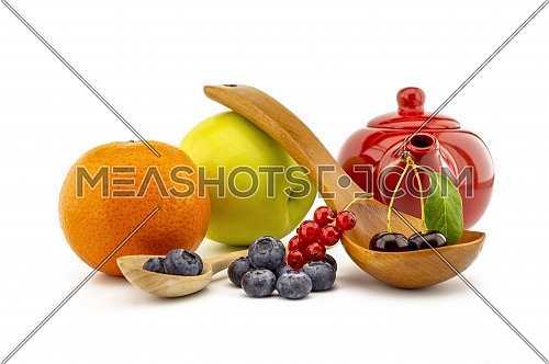 Fresh seasonal fruit still life with assorted berries including blueberries, cherries and red currants on wooden spoons with apple and orange and colorful red teapot