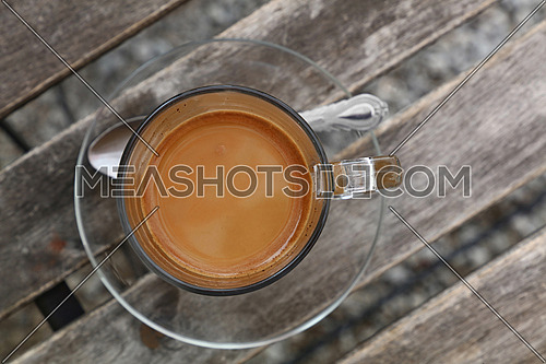 Turkish freshly brewed natural ground coffee with milk in transparent glass cup with saucer over vintage wooden table, detail close up, elevated top view