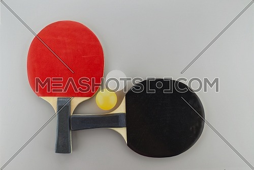 Two table tennis racks with a white and yellow ping pong ball on grey background
