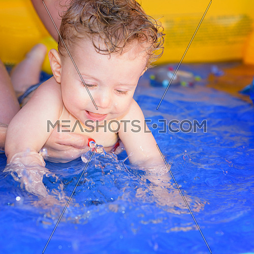Mom helps her baby to swim in a small paddling pool