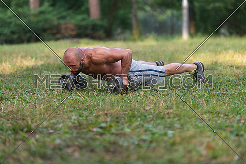 Young Muscular Athlete Doing Push Ups With Dumbbells As Part Of Bodybuilding Training - Outdoors Workout - Sports And Fitness - Concept Of Healthy Lifestyle - Fitness Male