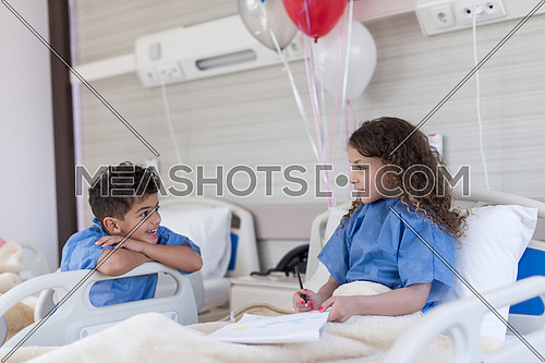 little middle eastern boy and girl painting home and family at hospital bed in a large modern hospital