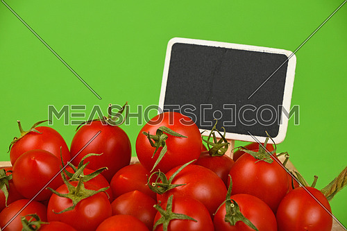 Red ripe fresh small cherry tomatoes with black wooden chalkboard price sign tag close up over green background