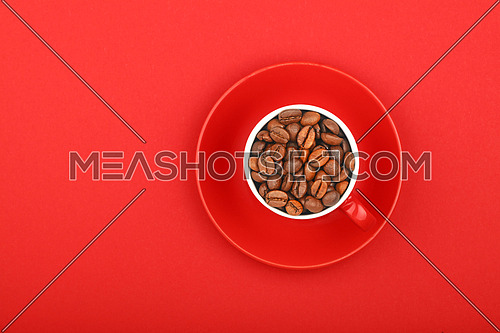One small red espresso cup full of roasted coffee beans, with saucer on red paper background, top view, bird eye view