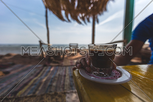 Close up for male hand holding coffee glass by the beach in Dahab, Egypt
