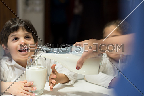little middle east boy and girl with mom eating snacks and drinking milk in the kitchen with pleasure