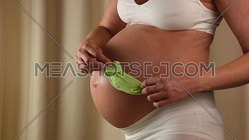 Close up profile view of pregnant Caucasian woman holding and touching her exposed belly with hands and playing with baby sock