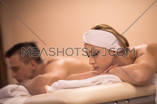 Portrait of relaxed beautiful young couple lying on massage table at spa center
