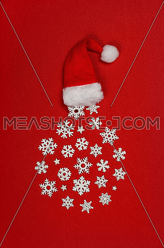 Close up circle of white wooden snowflake Christmas decoration out of red Santa hat over red felt background with copy space, table top view, flat lay