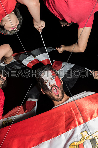 low angle for group of young people cheering for egypt, holding egyptian flags and drum while one of them has a paint egyptian flag on his face in the korba area at night
