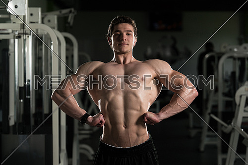 Young Man Standing Strong In The Gym And Flexing Muscles - Muscular Athletic Bodybuilder Fitness Model Posing After Exercises