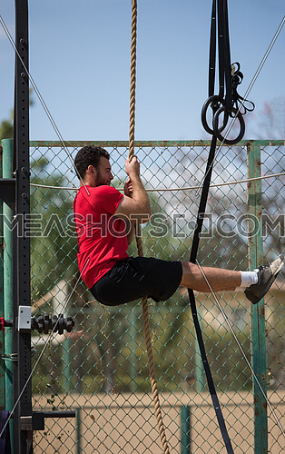 young middle eastern athletic man strenuous exercise climbing the rope outside on a sunny day