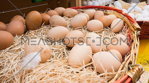 Brown chicken eggs leaning on straw in wooden basket at matket,outdoor.