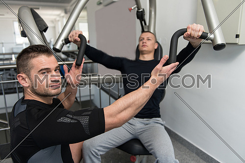 Personal Trainer Showing Young Man How To Train Chest On Machine In The Gym