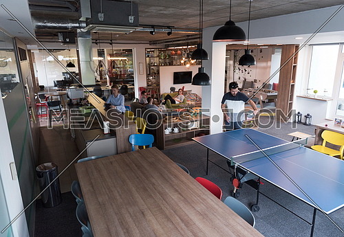 Two young start up business man playing ping pong tennis at modern creative office space  people group have meeting and brainstorming in background