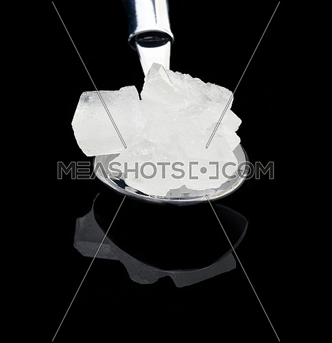 crystal sugar  on a spoon over black reflective surface background