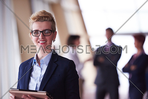 Smilling young business woman with tablet computer  in front her team blured in background. Group of young business people. Modern bright  startup office interior.