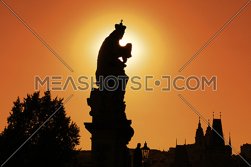 Sunset backlit silhouettes of statues and roofs of cityscape skyline at Charles Bridge in Prague, Czech Republic