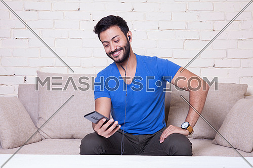 A young man sitting on a sofa using his Mobile Phone behind a white wooden table