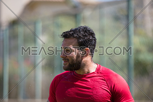 young middle eastern man is refreshed after a hard workout pouring water over themselves to summer heat