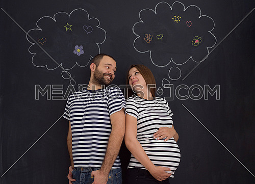 portrait of husband and pregnant wife posing against black chalk drawing board