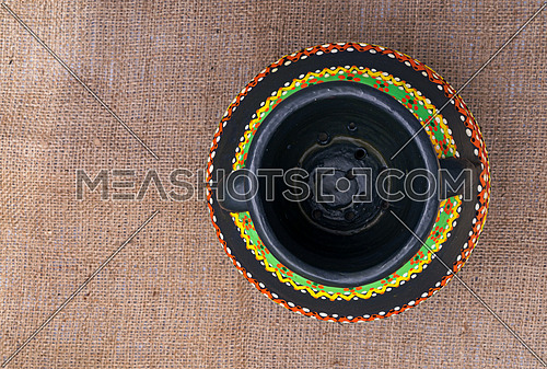 Top view of a black Egyptian handcrafted artistic pottery jar on a sackcloth background