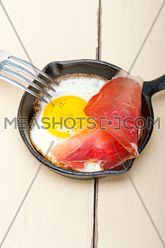 fried egg sunny side up with Italian tyrolean speck smoked ham on a skillet