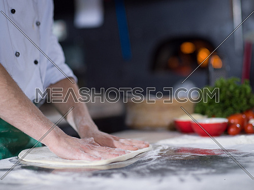 chef preparing dough for pizza rolling with hands on sprinkled with flour table