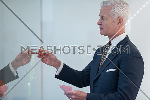 senior business man at modern office making plans and projects with post stickers on glass