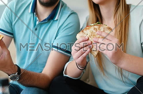 Young Couple Talking And Eating Chips and sandwiches On Sofa At Home