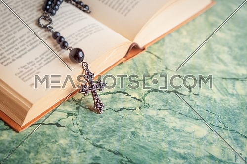 Black rosary and cross on the Bible on a green table. Religion at school.