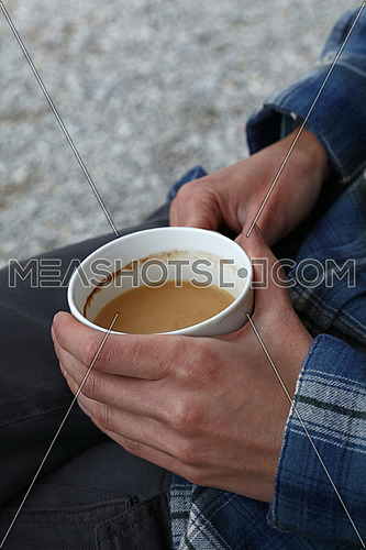 Close up woman sitting relaxed and holding cup of coffee with milk with two hands, high angle side view