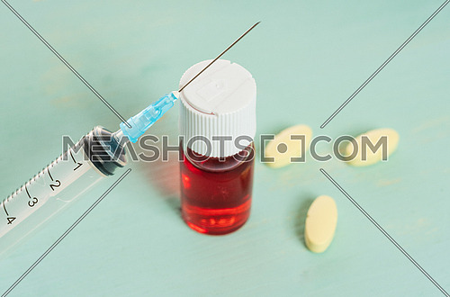 medical vaccine phials with red liquid, yellow tablet and syringe over green table and white background. Vaccination and immunization conceptual.