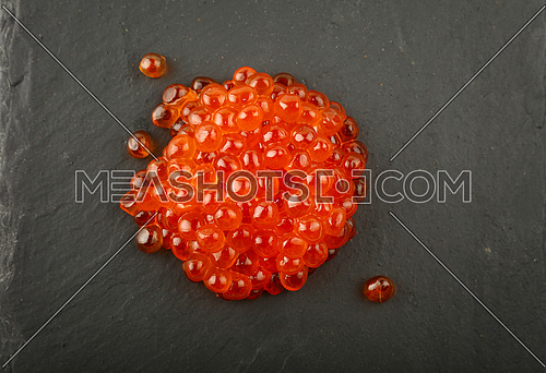 Close up one heap portion of salmon fish red caviar on background of black slate kitchen board, elevated top view, directly above