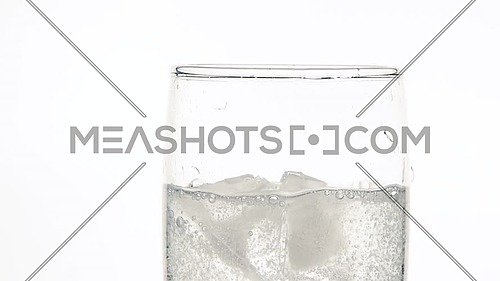 Close up dropping ice cubes in glass of pure clear sparkling water with gas over white background, low angle side view, slow motion