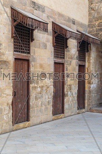 Facade of old abandoned stone bricks wall with three weathered wooden doors and opening covered with wooden grid, Old Cairo, Egypt