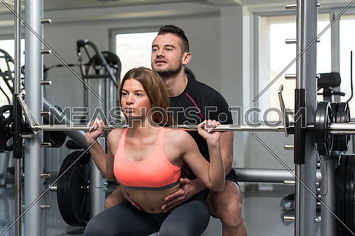 Personal Trainer Showing Young Woman How To Train Barbell Squats Exercise In A Health And Fitness Concept