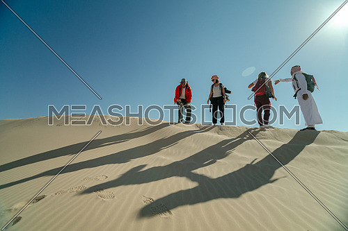 Group of tourists walking on sands with bedouin guide while exploring Sinai Trail in Ain Hodouda by day.