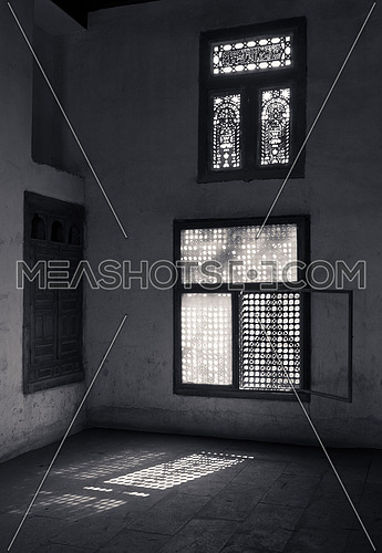 Old abandoned dark damaged dirty room with two wooden broken ornate windows covered by interleaved wooden grid (mashrabiya). Black and white shot