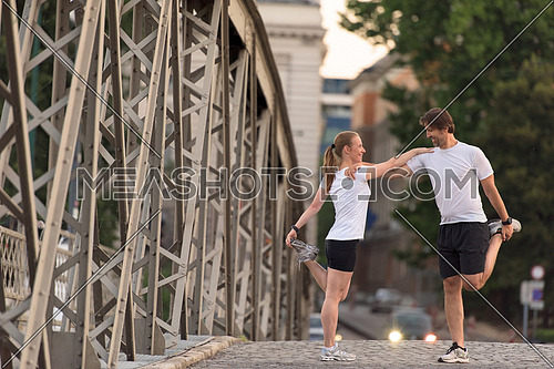 jogging couple warming up and stretching before morning running training workout  in the city with sunrise in background