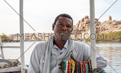 a Nubian man sitting by the nile selling accessories