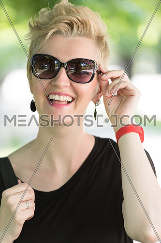 Beautiful fashionable young woman with short blond hair and sunglasses posing in the park