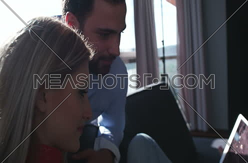 Pedestal shot for Sweet Couple while female is Using Tablet  On Couch and sun flares from window