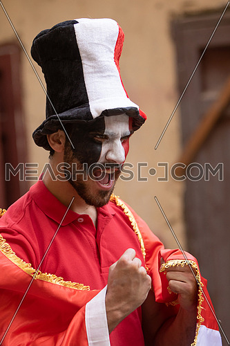 A male Egyptian fan painting a flag on his face wearing supporter's hat